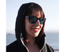 Woman smiling outdoors wearing Method Seven Coup HPS sunglasses with reflective lenses.