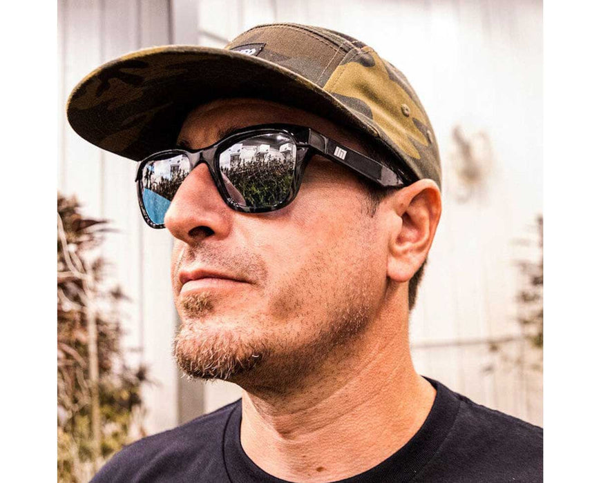 Man wearing Method Seven Coup HPS glasses and camouflage cap, standing near greenhouse.