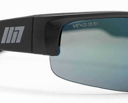Close-up of the Method Seven logo on the Cultivator FX2 glasses, showing lens edge detail and matte black finish.