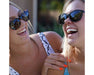 Two women laughing outdoors wearing Method Seven Lennox Sun Polarized sunglasses in a casual summer setting.