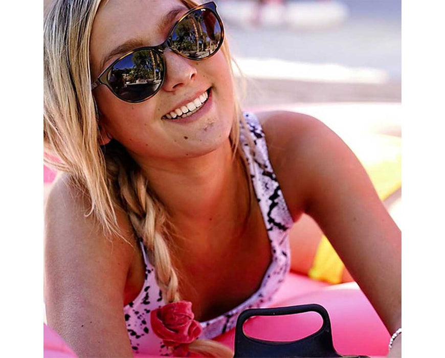 Smiling woman lounging outdoors in Method Seven Lennox Sun Polarized sunglasses, reflecting palm trees in the lenses.