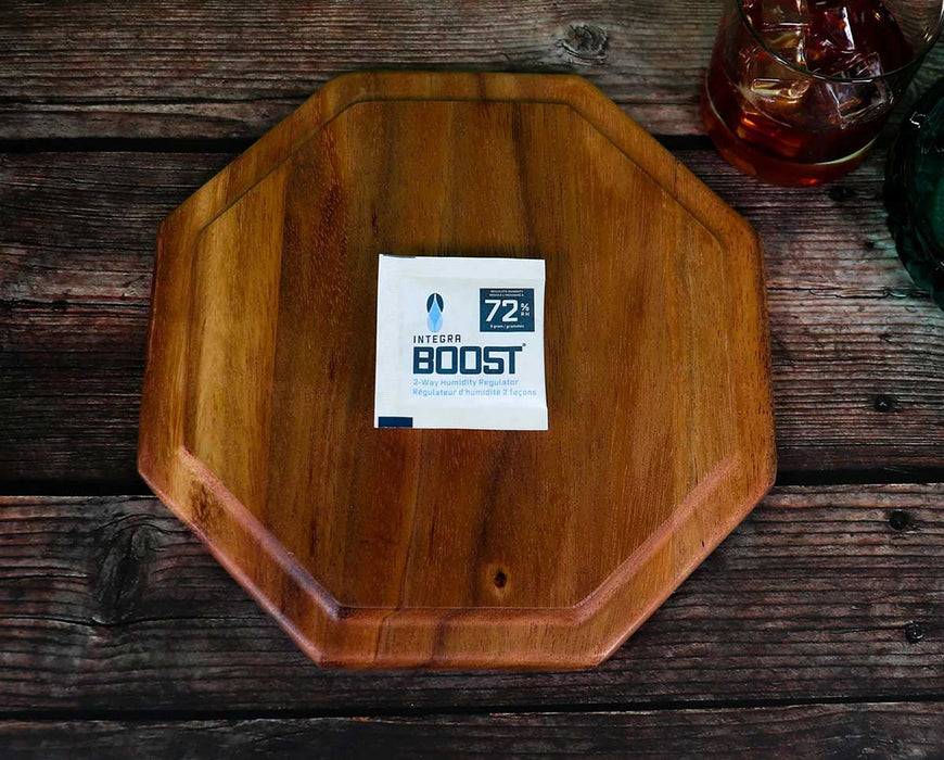 Integra BOOST 8g 72% RH humidity control pack placed on wooden tray beside a drink and glass ashtray.