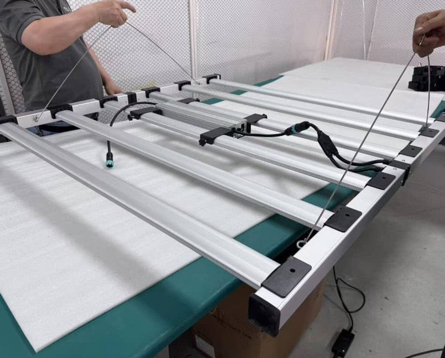 Technicians assemble Nova Sun Series LED grow light, attaching suspension wires for overhead installation in grow space.