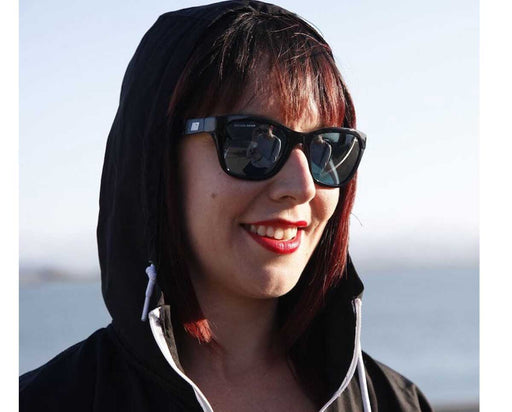 Smiling woman wearing Method Seven Coup HPS Premium sunglasses outdoors by the sea.