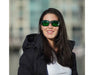 Smiling woman outdoors wearing Method Seven Operator LED glasses with green lenses and black frame.